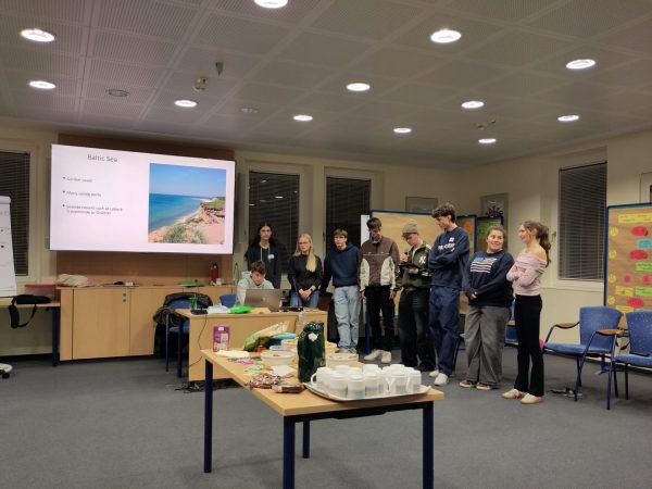 Tourismuspräsentation im Plenum auf einem großen Bildschirm. Ein Schüler sitzt davor am Laptop und acht Schülerinnen und Schüler stehen rechts daneben.