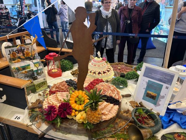 Eine Festtagstafel mit Aufschnitt, Früchten und einer Torte, daneben ein Jäger-Magazin und ein Willkommensschild.