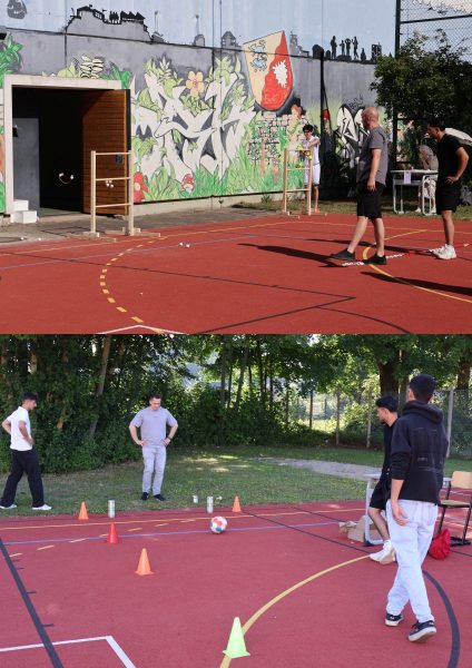 Oben: Auf einem roten Sportplatz mit gelben Spielfeldmarkierungen stehen mehrere Jugendliche und ein Erwachsener in sportlicher Freizeitkleidung. Im Hintergrund ist eine Wand mit großflächigem Graffiti und einem Wappenmotiv zu sehen. Eine offene Tür führt in ein Gebäude. Unten: Mehrere Jugendliche stehen auf demselben Sportplatz und nehmen an einer Aktivität mit einem Fußball teil. Der Ball liegt zwischen orangefarbenen Hütchen, die einen Parcours markieren. Im Hintergrund stehen Bäume und ein Zaun, die Szene wirkt sommerlich und entspannt. Die Aufnahme dokumentiert Aktivitäten beim Sport- und Spielevent der Berufsvorbereitungsklassen am BBZ am NOK.